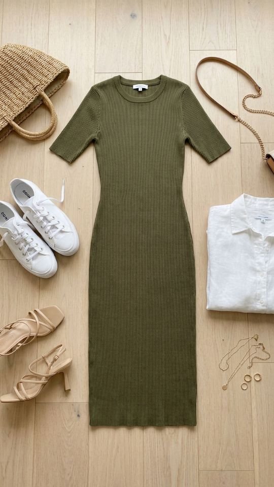 photo of a flat lay showing one olive ribbed midi dress laid flat in the centre with white sneakers, nude heeled sandals, a straw bag, a small chain bag, and a folded white shirt arranged around it, set on a pale wooden floor, with soft even natural light from above, organised and satisfying mood, and details including thin gold jewellery placed in one corner.